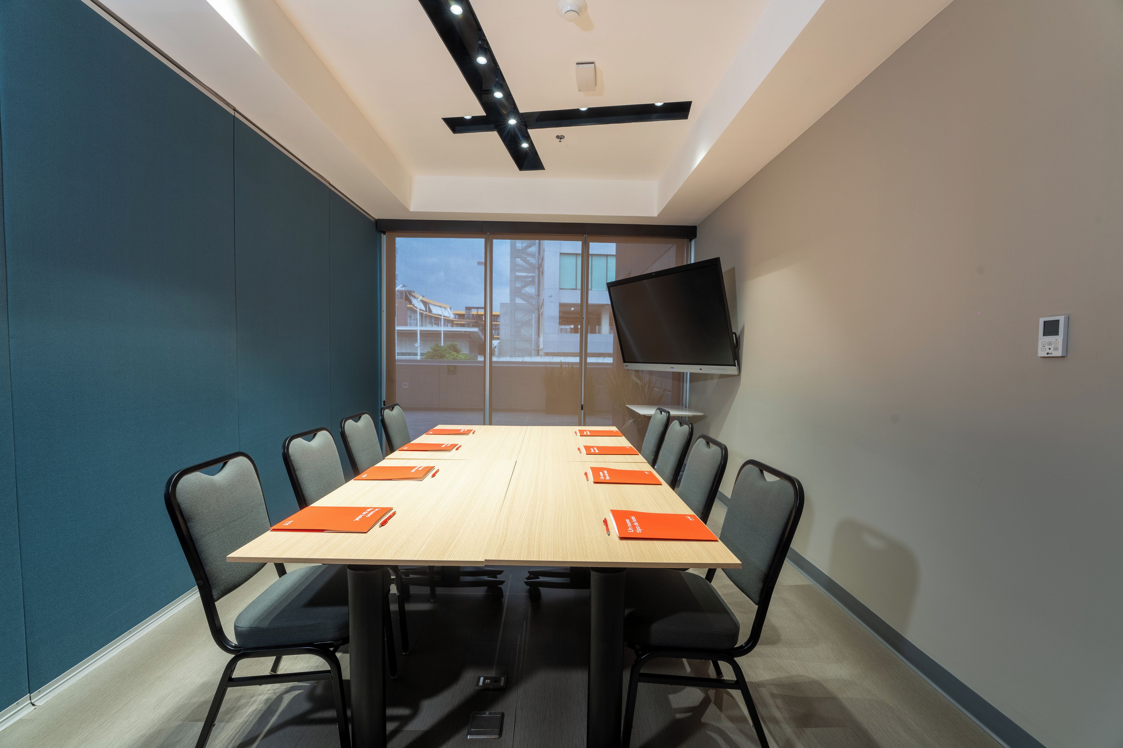 Une salle de conférence équipée d’une longue table, de chaises, d’un téléviseur à écran plat et d’une fenêtre donnant sur des immeubles.