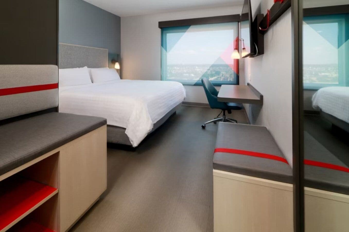 A hotel room with a bed, a desk, a chair, and a TV mounted on the wall.