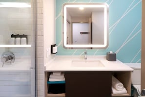 Un baño moderno con un lavamanos blanco, un espejo con luz y un perchero para toallas.