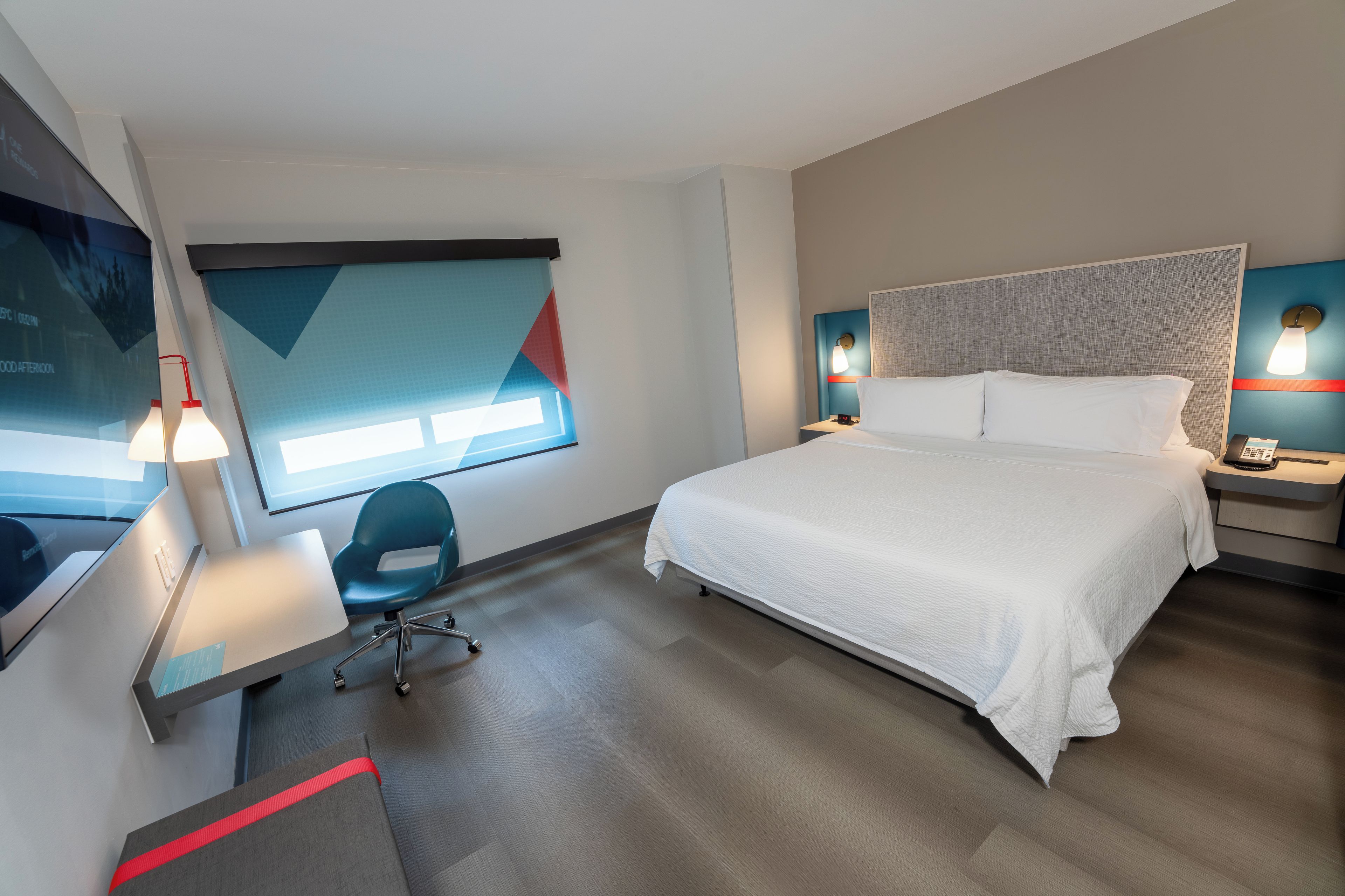 Une chambre d’hôtel équipée d’un lit, d’un bureau, d’une chaise, d’une télévision et d’une fenêtre donnant sur un paysage agréable.
