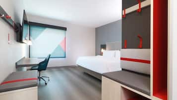 A modern hotel room with a bed, desk, and chair, a TV mounted on the wall, and a large window.