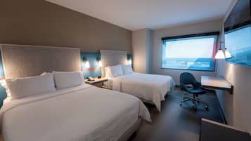 Une chambre d’hôtel avec deux lits, un bureau, une chaise et une grande fenêtre donnant sur la ville.