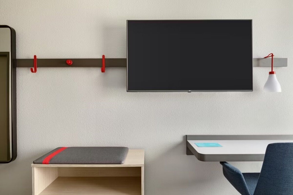 A modern room with a mounted TV, a desk with a chair, and a small shelf.
