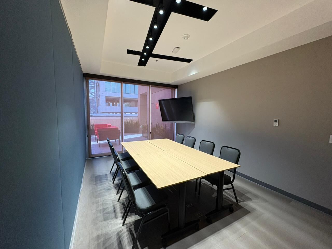 A conference room with a long table, chairs, a flat-screen TV, and a large window.