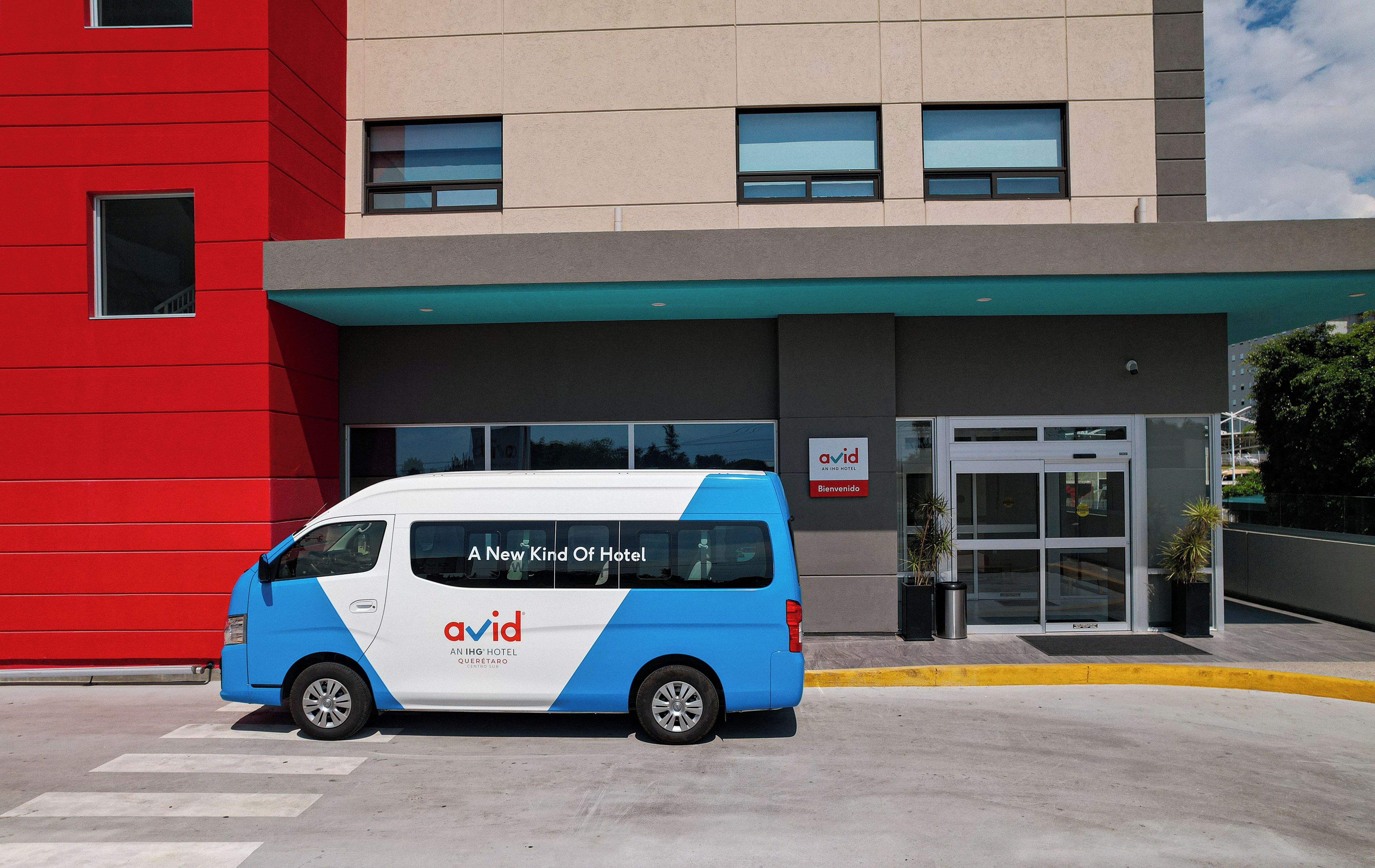 A blue and white van parked in front of a hotel with a red building on the left.