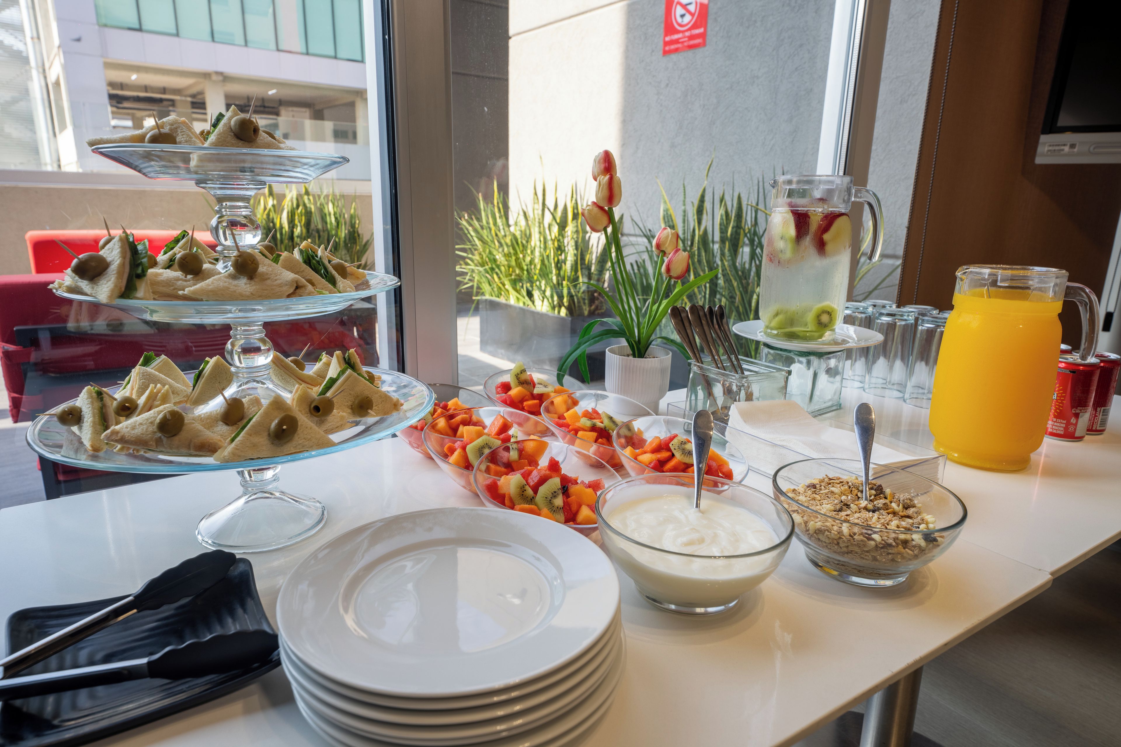 Una mesa de buffet con diferentes alimentos, como sándwiches, fruta y una jarra de jugo.