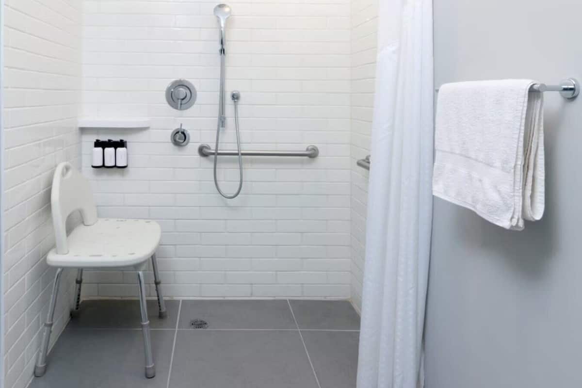 A small, white, tiled bathroom with a shower, a toilet, and a towel rack.