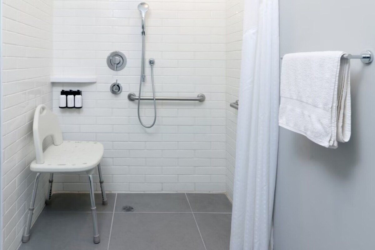 A small, white, tiled bathroom with a shower, a toilet, and a towel rack.