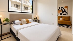 Egy modern hálószoba, amelyben egy nagy ágy, éjjeliszekrények, egy virágos növény és egy ablakból nyíló kilátás látható egy épületre.