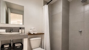 Egy modern fürőszoba, amelyben WC, mosdókagyló és zuhanyzó található.