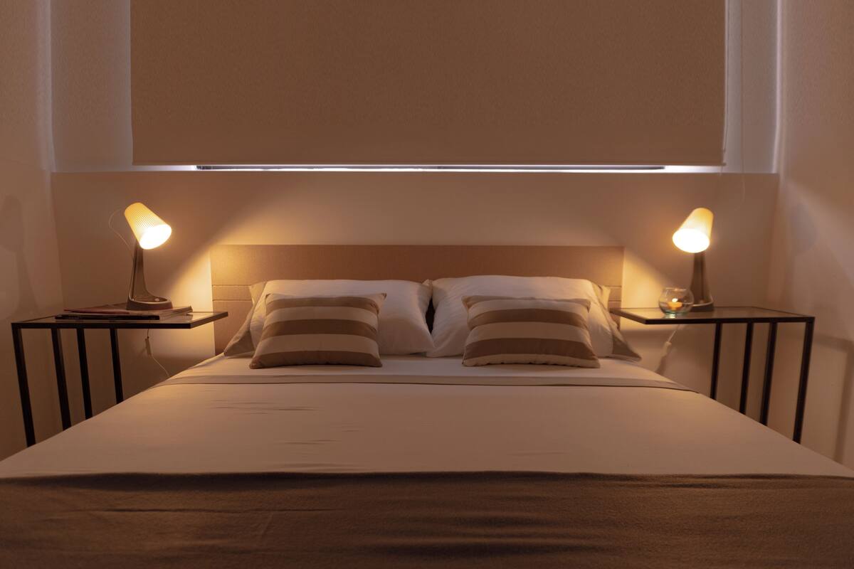 A neatly made bed with two pillows and two bedside tables with lamps.