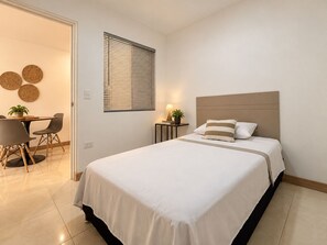 A hotel room with a bed, bedside table, lamp, and a dining area with chairs and a table. - Apartasuites ISABEL (Cali)