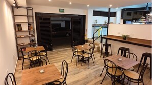 A modern dining area with wooden tables and chairs, a staircase, and a view of the street. - Apartasuites ISABEL (Cali)
