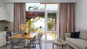 A modern kitchen with white cabinets, a dining area with a wooden table and chairs, and a view of the sea through large windows. - Votsalo Ierapetra (Ierapetra)