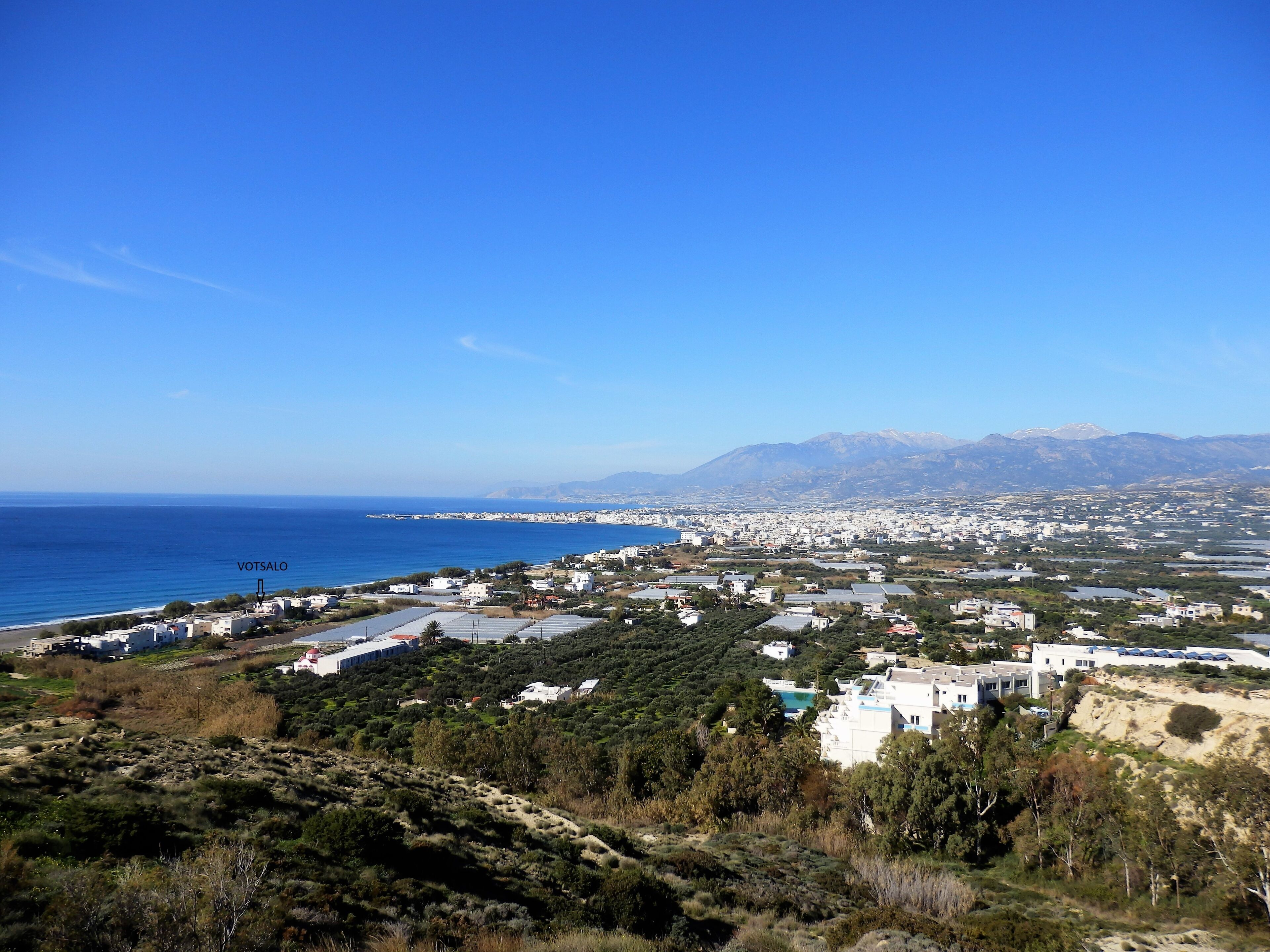 A coastal town with buildings, a beach, and mountains in the background.