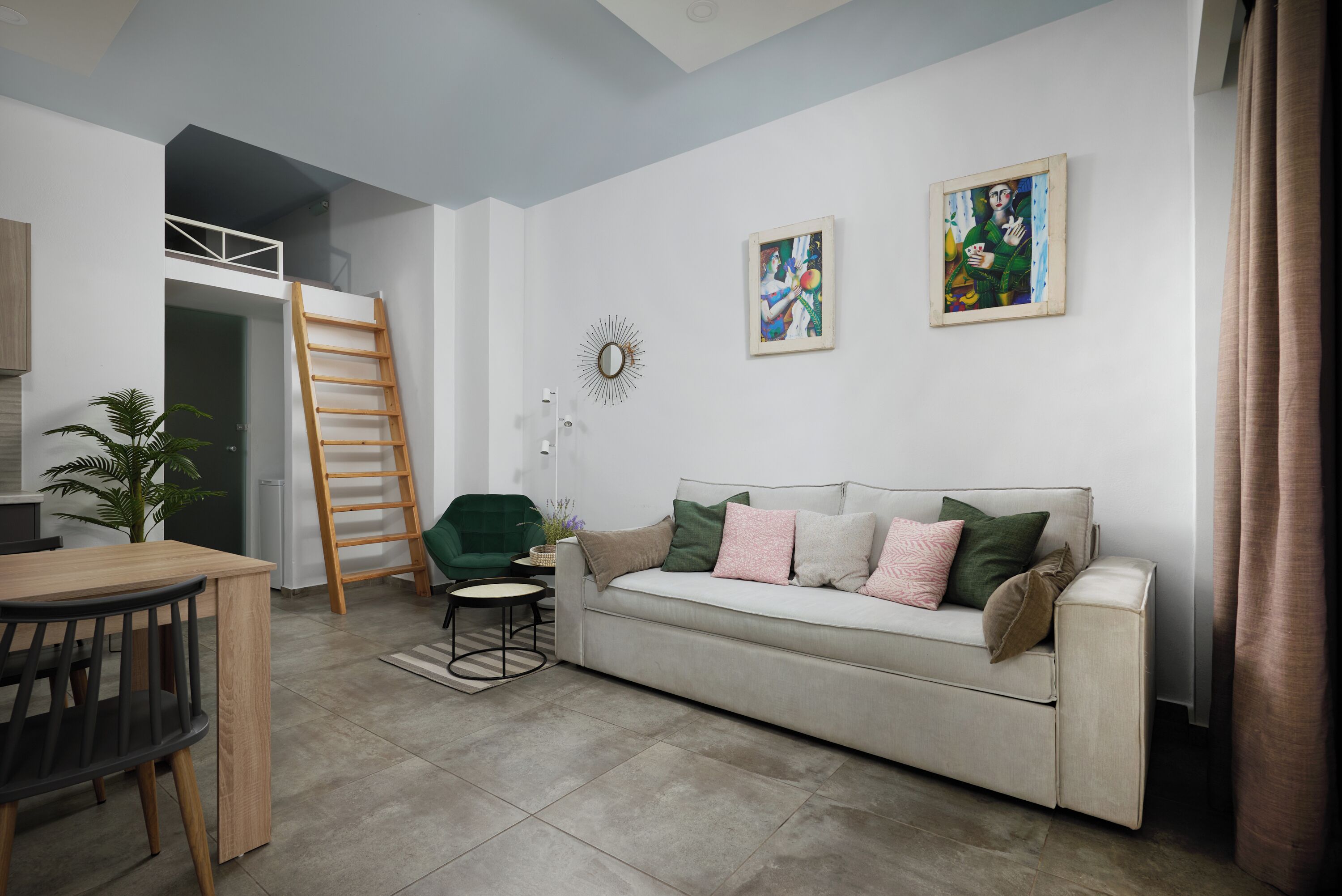Un salon moderne avec un canapé, une table à manger, une échelle et deux œuvres d’art encadrées accrochées au mur.
