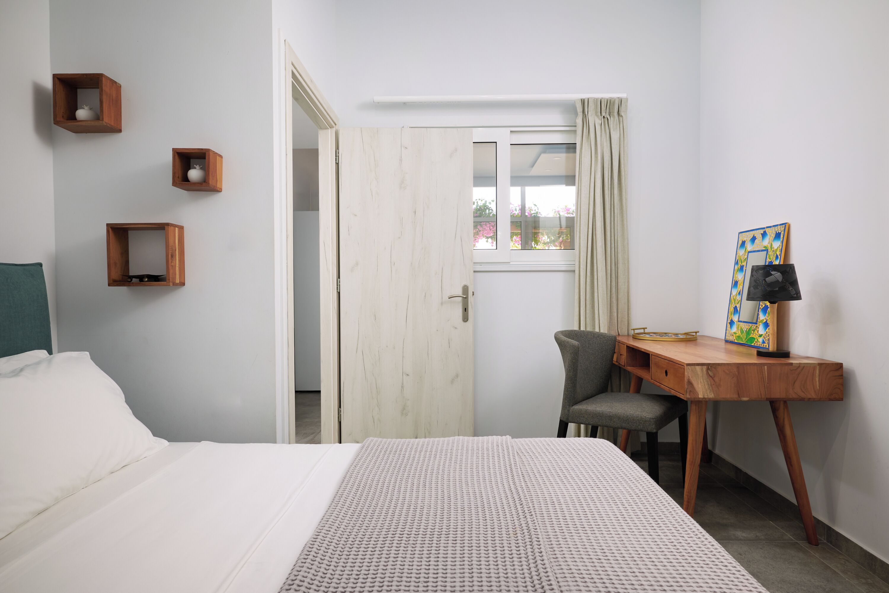 A bedroom with a bed, a desk, a chair, and a door leading to another room.