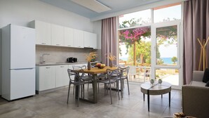A modern kitchen with white cabinets, a dining table with chairs, and a view of the sea through large windows. - Votsalo Ierapetra (Ierapetra)