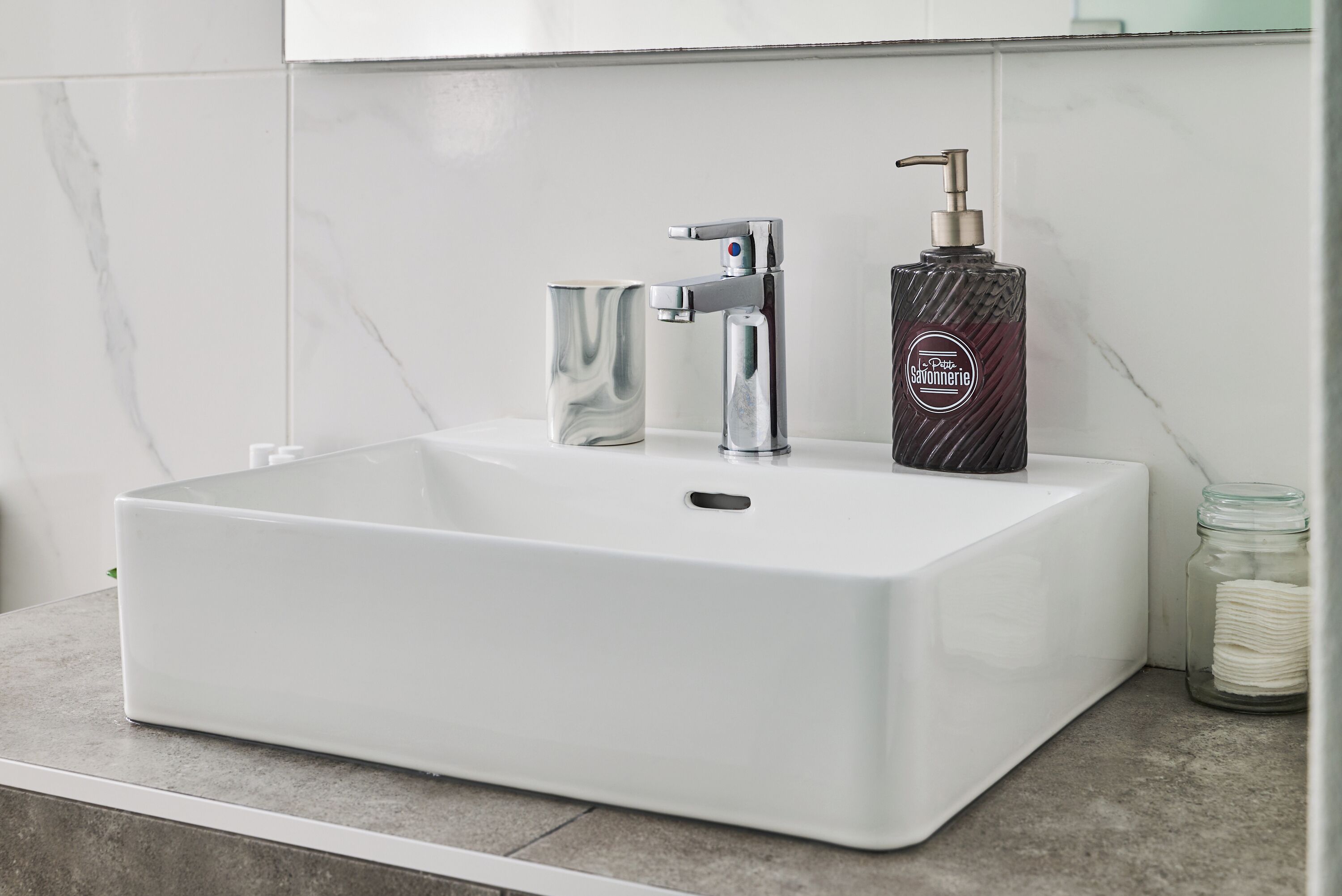 Un lavabo rectangulaire blanc pour salle de bain, doté d’un robinet moderne et d’un distributeur de savon.