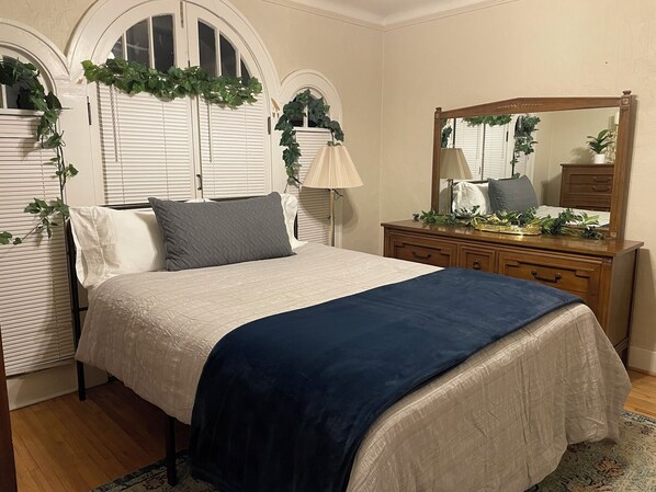 A bedroom with a bed, dresser, mirror, and decorative plants. - The Wildflower w/ 2 Kitchens & Laundry in Central, Safe, Spotless 1920s Bungalow (Sioux Falls)