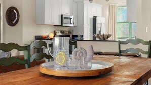 Een houten eettafel met een dienblad waarop een waterkan, glazen en een decoratief object staan. In de achtergrond zijn witte kasten en een magnetron zichtbaar.
