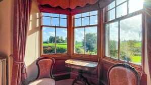 Une pièce d’angle avec deux fauteuils anciens, une petite table et une vue sur un paysage verdoyant, visible à travers de grandes fenêtres.