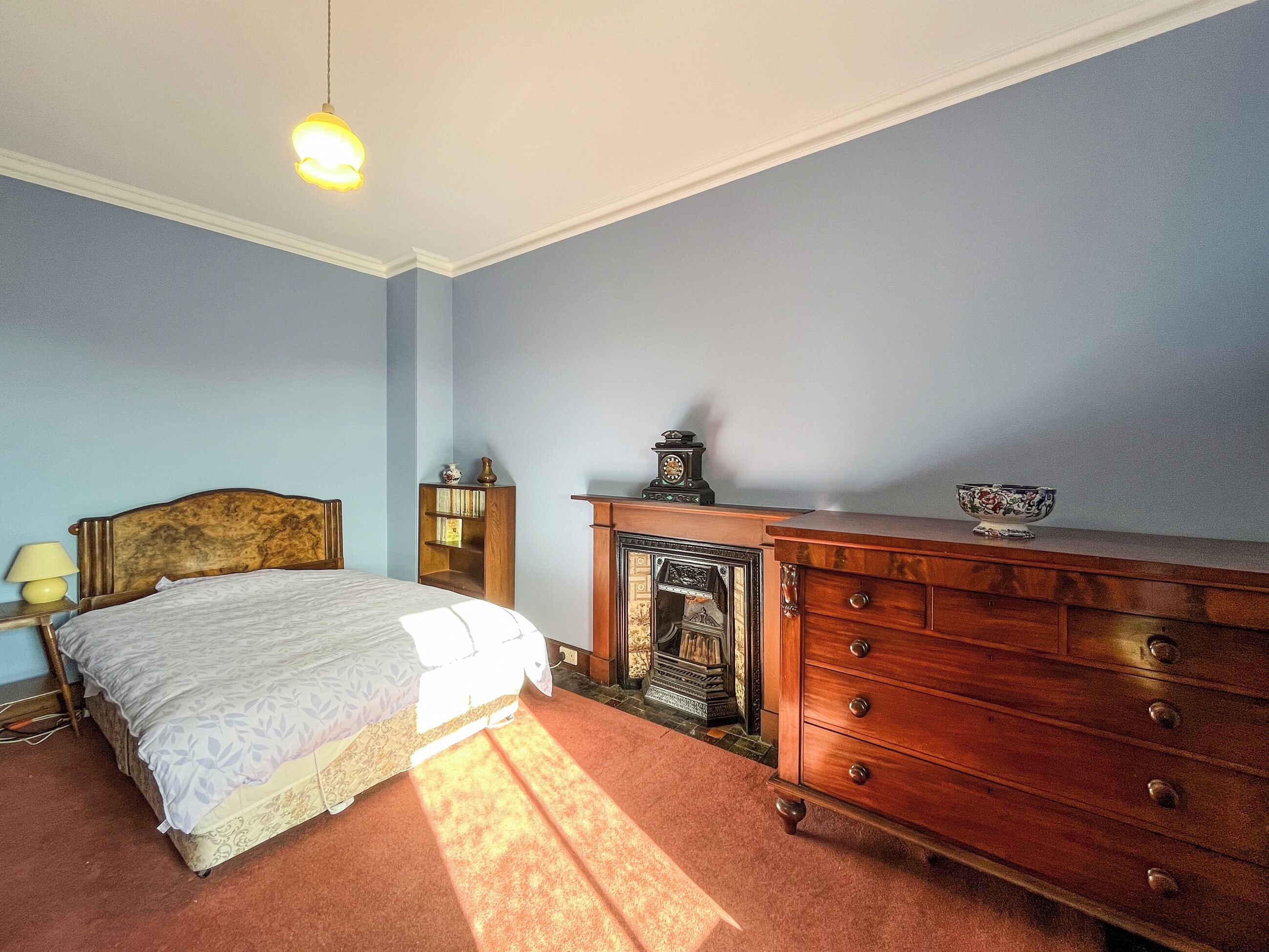Ein Schlafzimmer mit Bett, Schminktisch, Nachttisch, Lampe und einer Wanduhr.