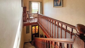 Un escalier en bois avec une rampe, une fenêtre avec des rideaux et un tableau accroché au mur.