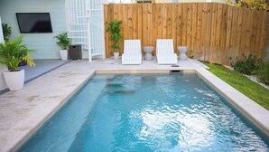 Une piscine rectangulaire avec deux chaises longues et une clôture en bois en arrière-plan.