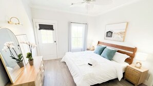 Une chambre à coucher avec un lit en bois, une table de chevet, une commode, un miroir et une fenêtre avec des rideaux.