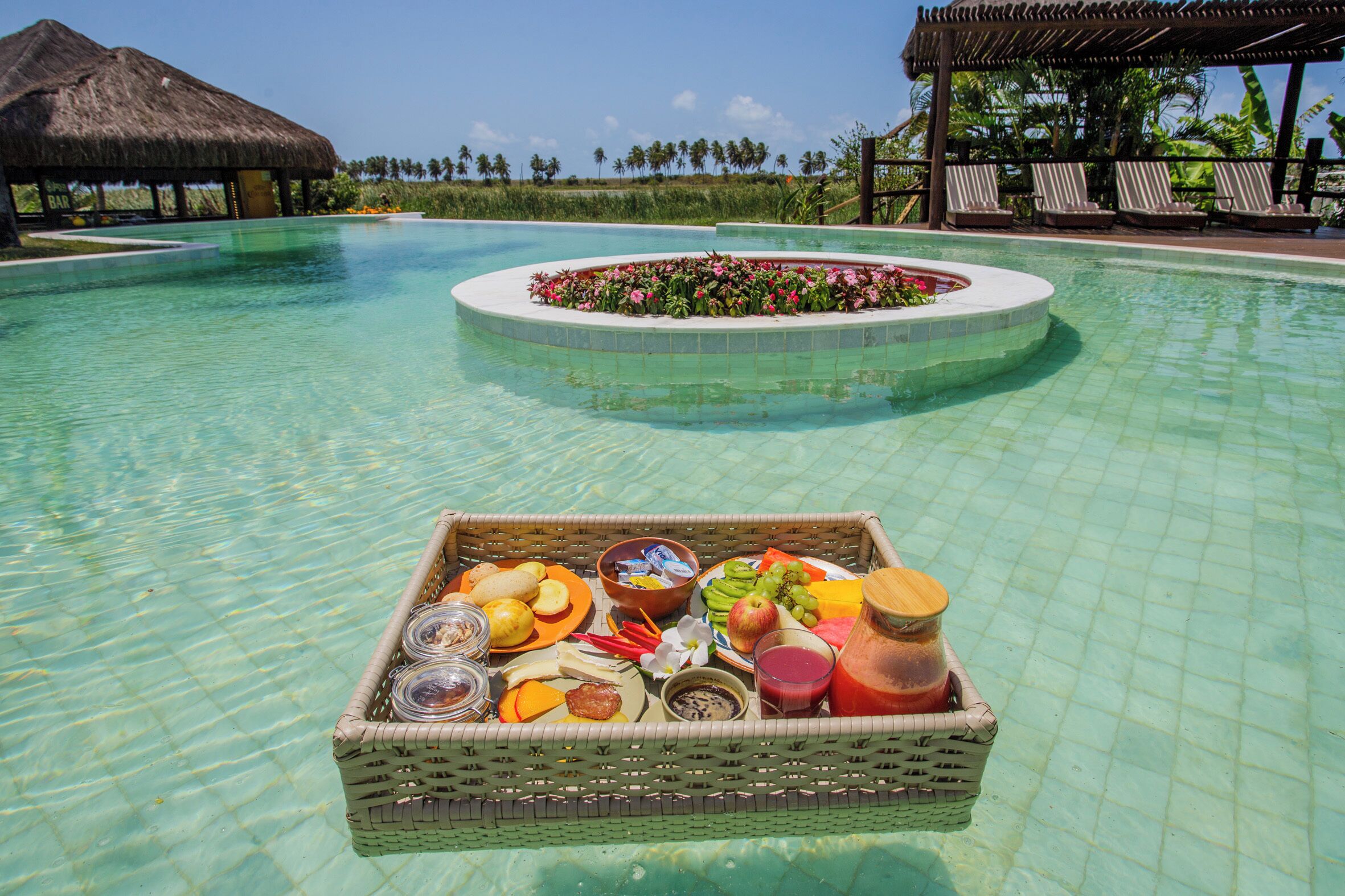 A poolside breakfast setup with a wicker basket containing fruits, bread, and beverages.