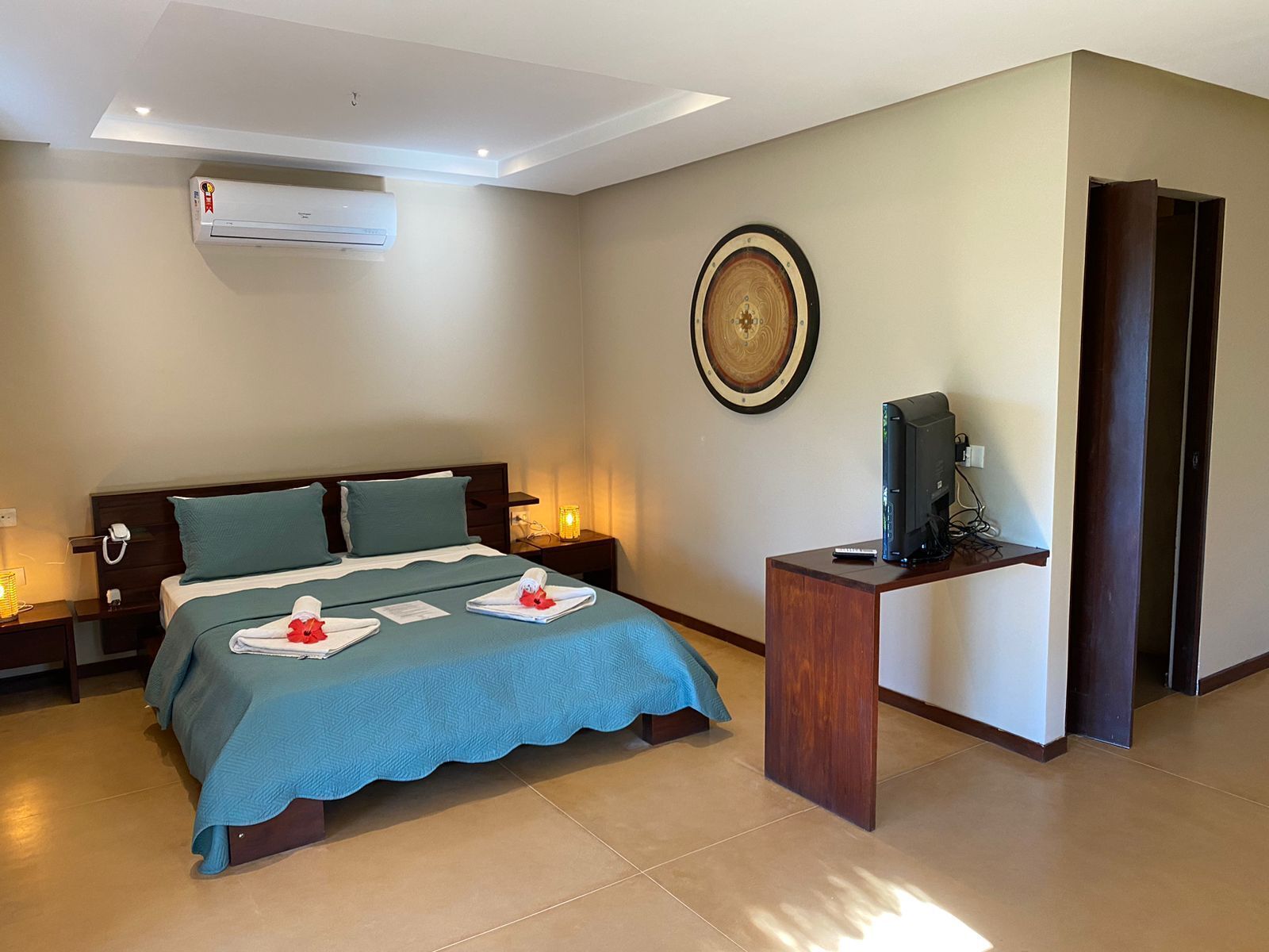 Habitación de hotel con cama, mesitas de noche, aire acondicionado, televisor y un adorno en la pared.