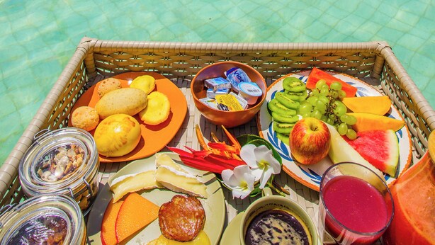 A tropical resort poolside setting with a buffet table featuring fruits, vegetables, and beverages. - Pousada Jaya Boutique (São Miguel do Gostoso)