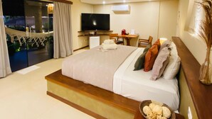 A modern hotel room with a large bed, a flat-screen TV, a small desk, and a balcony with a view. - Pousada Jaya Boutique (São Miguel do Gostoso)