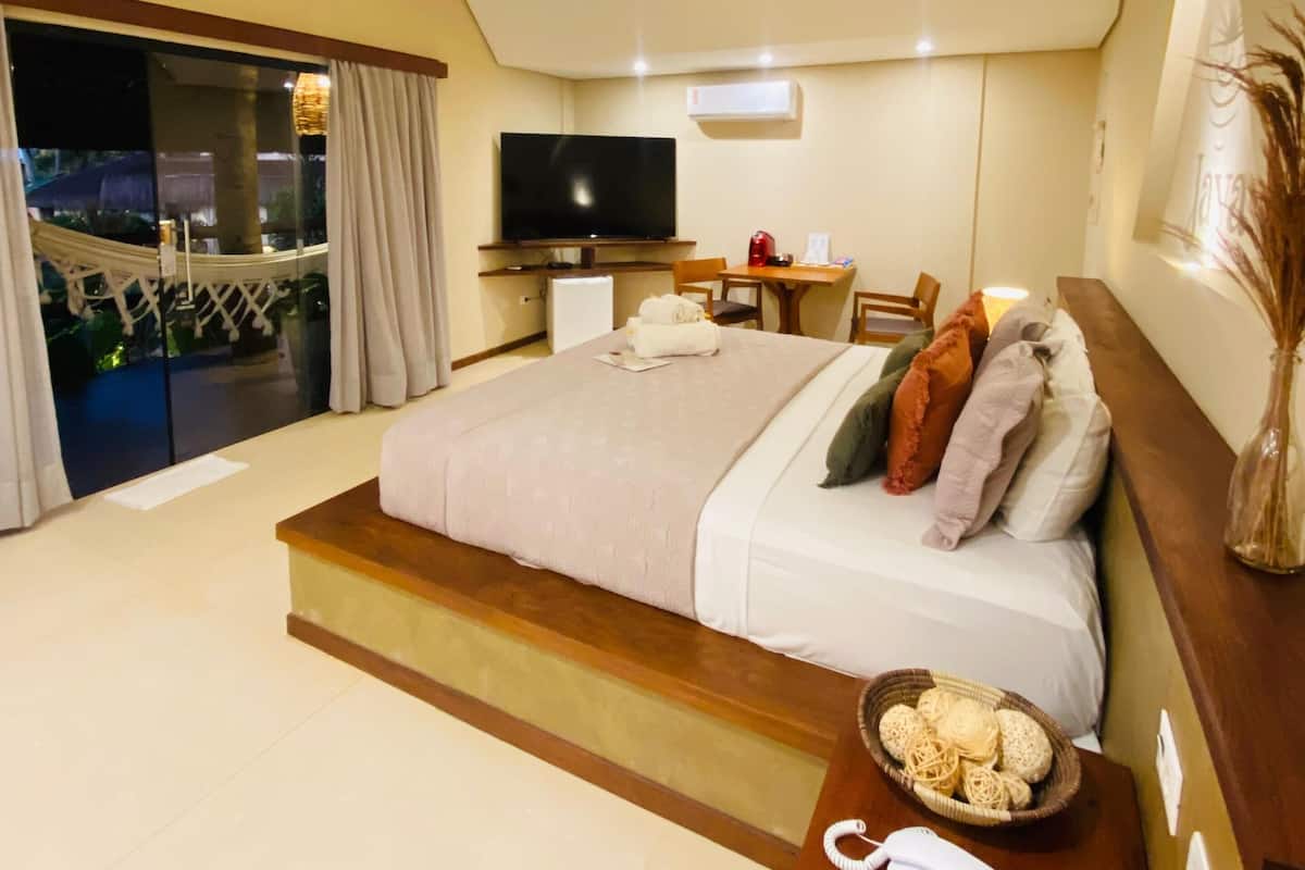 Quarto de hotel moderno com uma cama grande, uma TV de tela plana, uma pequena escrivaninha e uma varanda com vista.