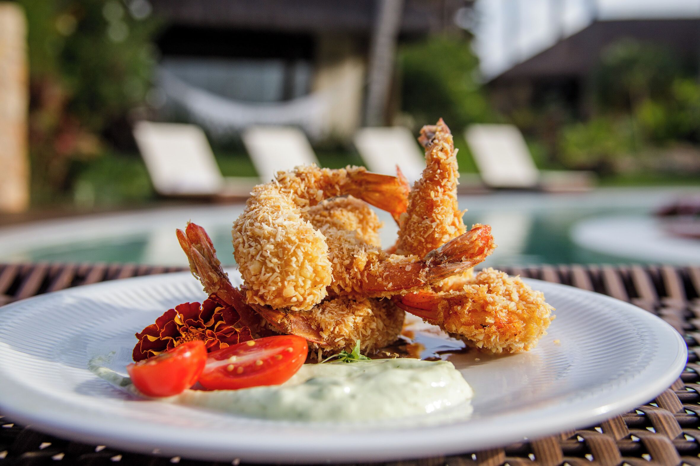 A plate of breaded shrimp with a side of sauce and a tomato slice.