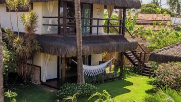 A two-story house with a thatched roof, a small pond, and a hammock.