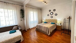 Camera da letto con due letti, pavimento in legno, comodino con lampada e pianta pensile.