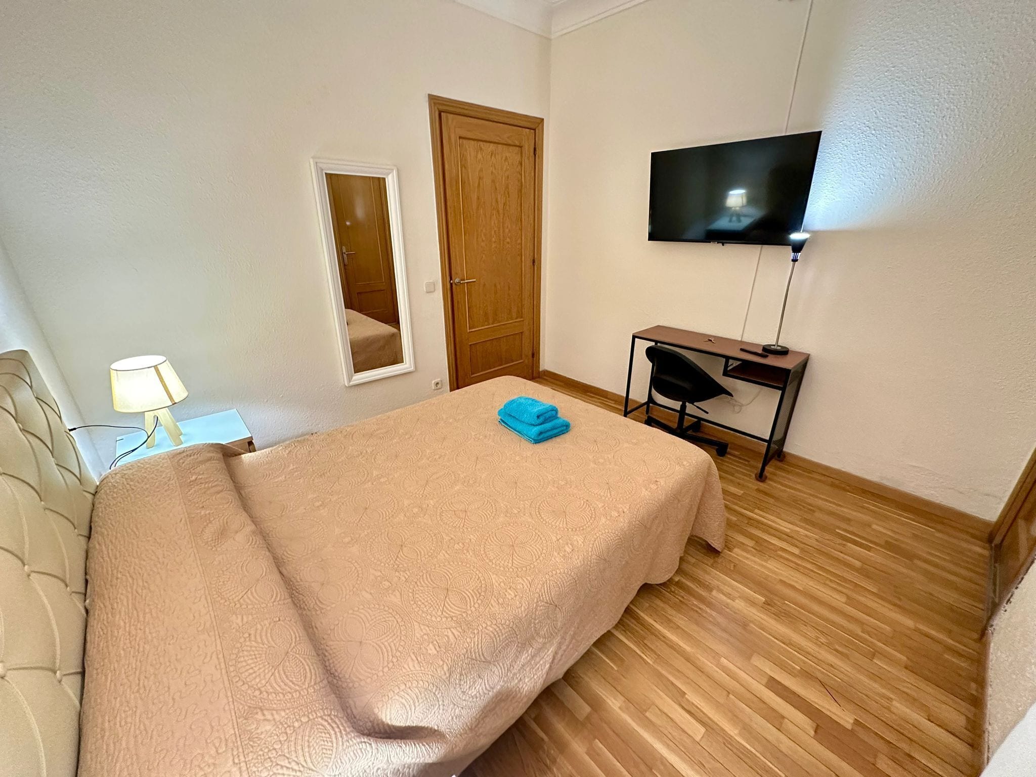 A hotel room with a bed, a desk, a chair, a TV, and a door.