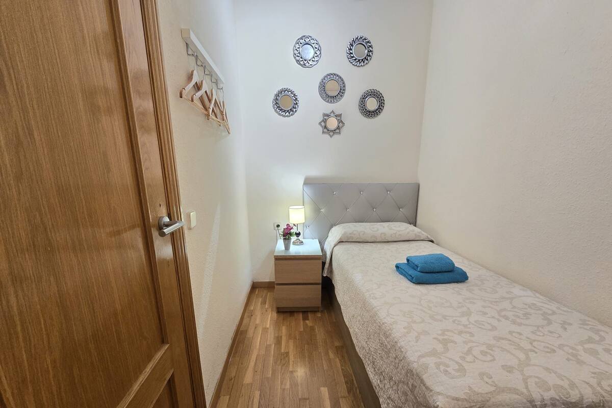 A small, neatly arranged bedroom with a bed, bedside table, and wall decorations.