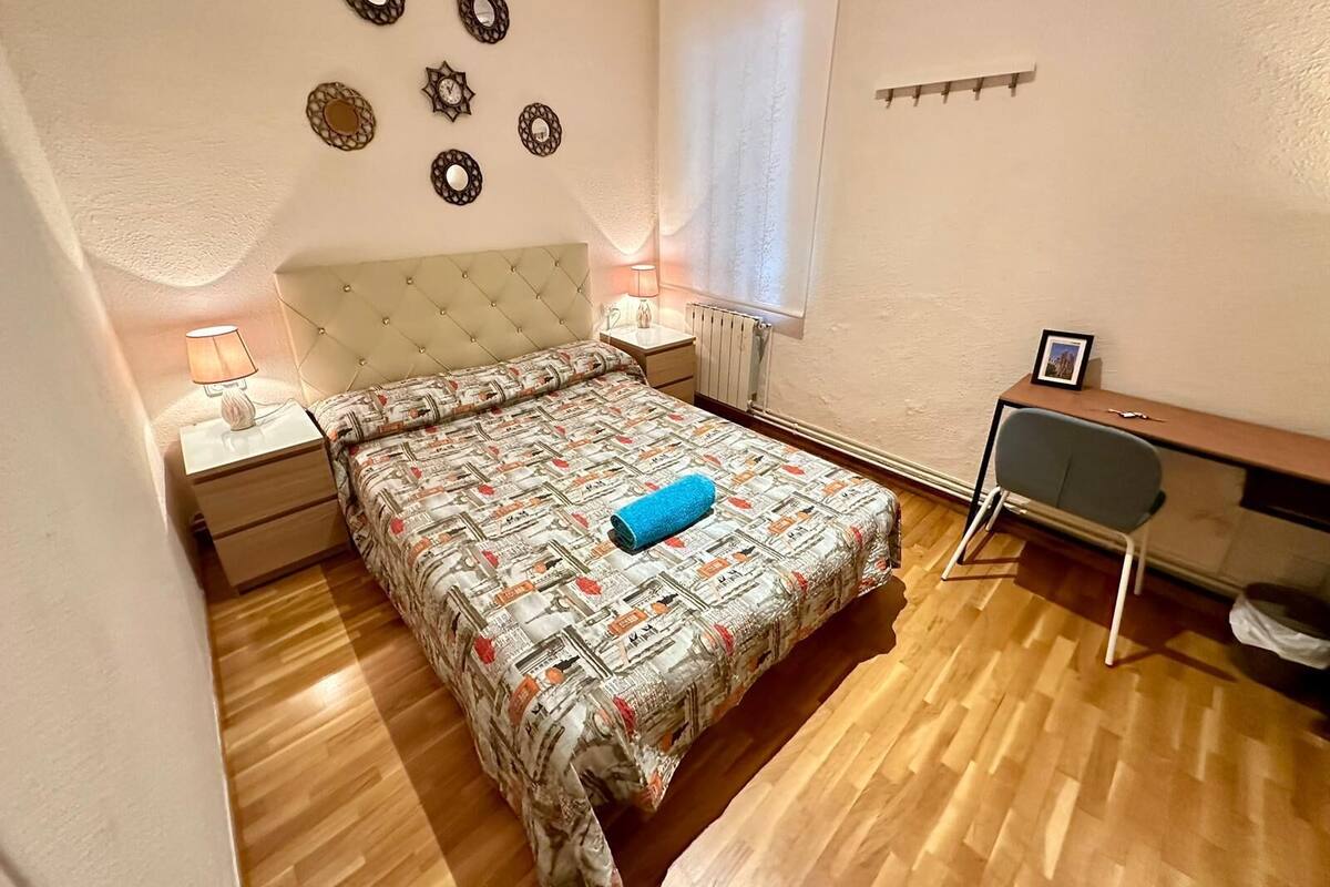 A bedroom with a bed, a desk, a chair, a nightstand, a lamp, and wall decorations.