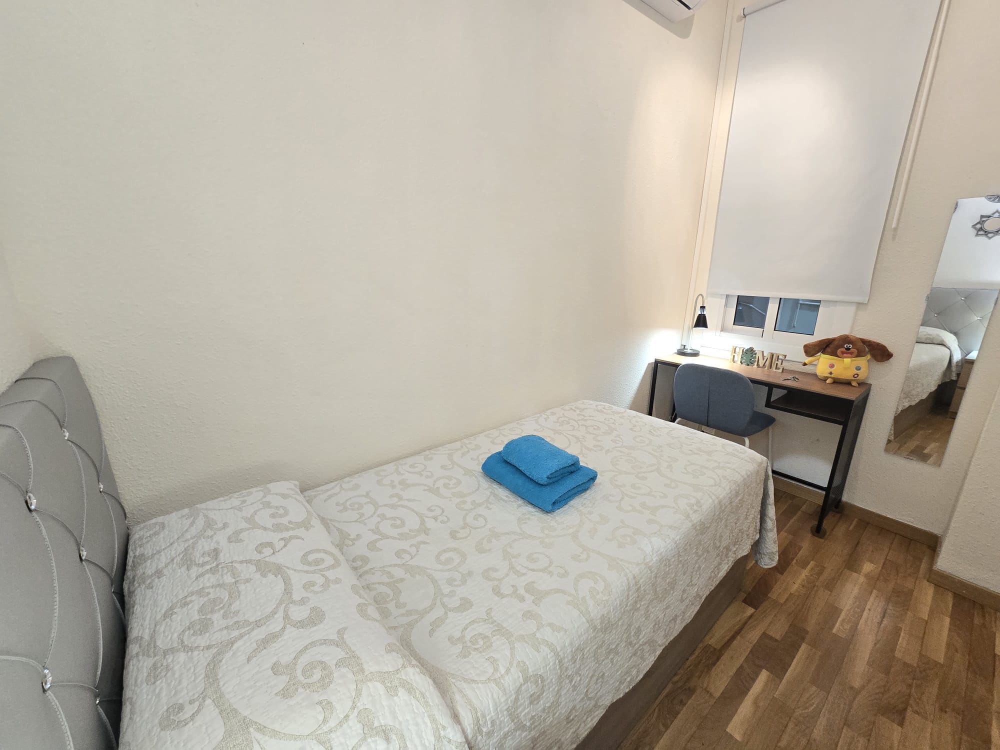 Une petite chambre à coucher, bien rangée, avec un lit, un bureau et une chaise.