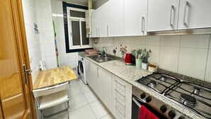 Una cucina compatta con mobili bianchi, un fornello a gas, un lavello e un tavolo di legno.
