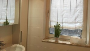 A bathroom with a bathtub, a sink, and a window with a curtain. - House Nicole vacation apartment 1 (Cuxhaven)