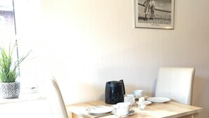 A dining area with a wooden table, white chairs, a black coffee pot, and a framed picture on the wall. - House Nicole vacation apartment 3 (Cuxhaven)