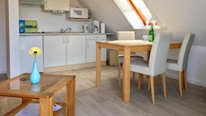 A compact kitchen with white cabinets, a microwave, and a coffee maker. There is a dining table with chairs and a small vase with a flower. - House Nicole vacation apartment 5 (Cuxhaven)
