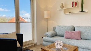 A living room with a grey sofa, a black armchair, a wooden coffee table, and a floor lamp. There are bookshelves with books and decorative items on the wall. - House Nicole vacation apartment 5 (Cuxhaven)