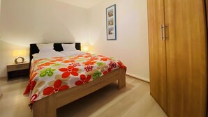 Een slaapkamer met een bed, nachtkastje, houten garderobe en een lijst met een afbeelding aan de muur.