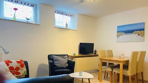 Een woonkamer met een zwarte bank, een kleine tafel, een televisie en een eethoek met stoelen.