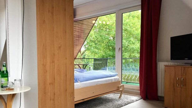 A bedroom with a bed, a TV, a wooden cabinet, and a window with a view of greenery. - House Nicole vacation apartment 10 (Cuxhaven)